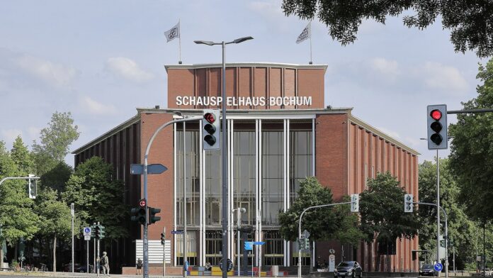 Das Schauspielhaus Bochum mit Backsteinfassade und Schriftzug, davor eine Kreuzung mit Ampeln